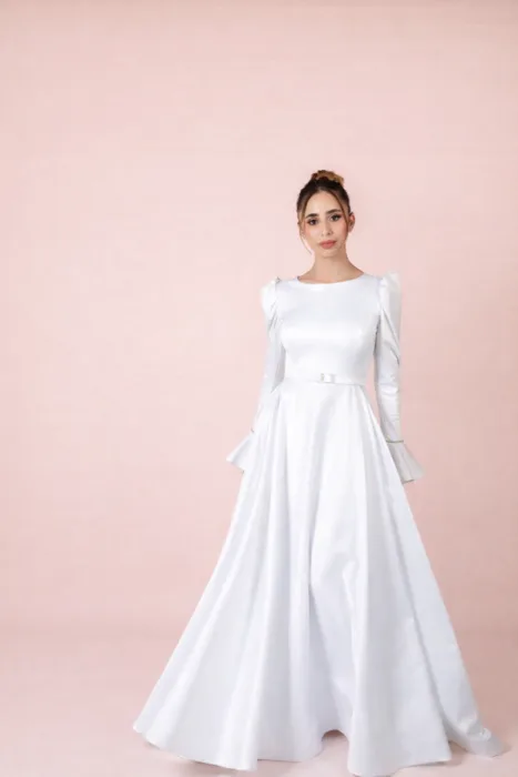 שמלת כלה אלגנטית בגזרה קלאסית ונקייה. שרוולים ארוכים עם נפח עדין בכתפיים וחגורה דקה במותן. חצאית מתרחבת באלגנטיות עד הרצפה למראה יוקרתי וצנוע. ✨